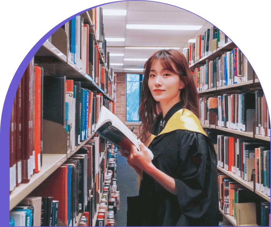 A graduate holding an open book between library shelves