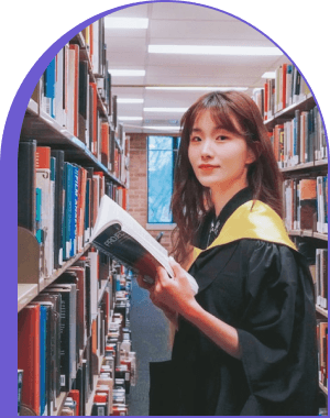 A graduate holding an open book between library shelves